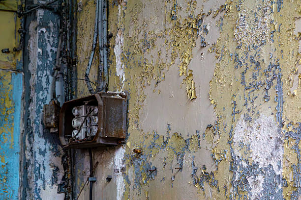 istock Old electrical box with porcelain fuses mounted on a wall with peeling paint and visible moisture damage in an abandoned industrial building. 2221881308
