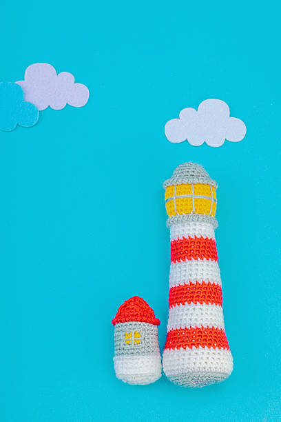 Handmade crochet lighthouse on blue background with clouds. Minimalist nautical-themed flat lay