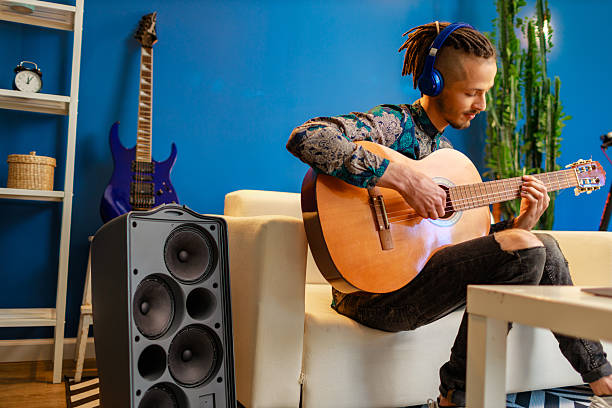 istock Young caucasian man with dreadlocks sitting on sofa and playing acoustic guitar 2221888956