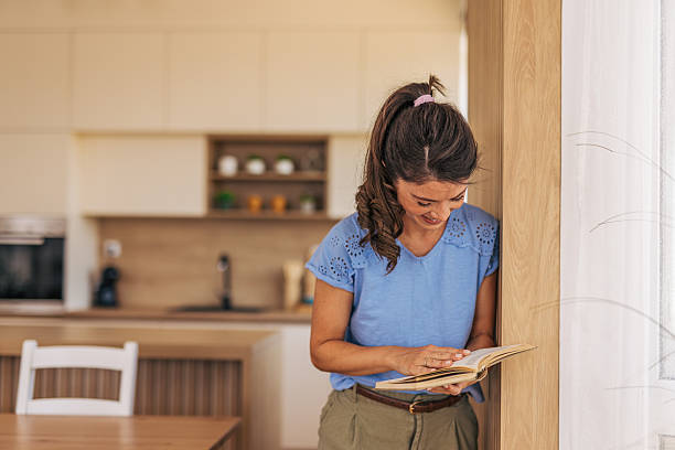 istock Young woman reading a book and smiling in her kitchen 2221892327