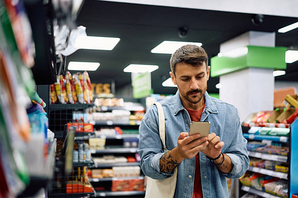 istock Mid adult man using reminder on cell phone while buying in supermarket. 2221916639