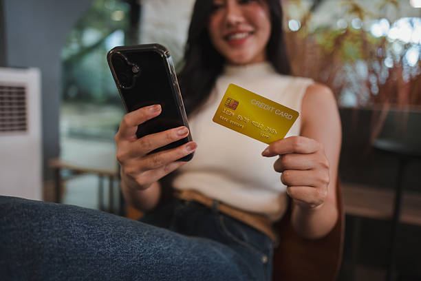 istock Smiling young woman holding a credit card while using a smartphone app for seamless online shopping and secure transactions 2221919074