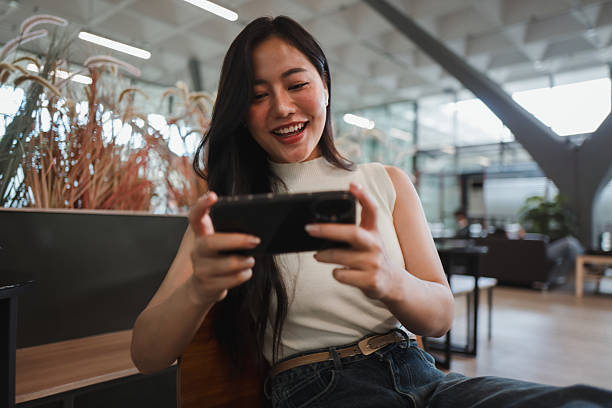 istock Young Asian office worker enjoying a break while playing a mobile game on her smartphone, smiling and having fun in a casual setting 2221919084