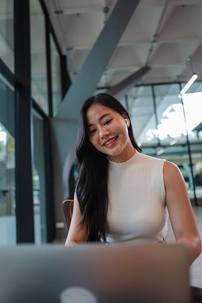 istock Young Asian woman working remotely using her laptop and smiling, enjoying flexible work arrangements in modern office space 2221919103