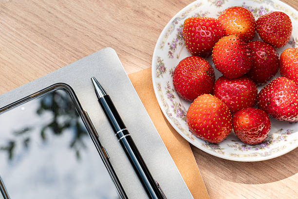 Strawberries, smartphone, and office supplies on wooden table, vibrant freelance workday scene