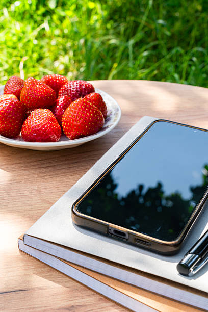 Bowl of strawberries and smartphone with pen on table outdoors