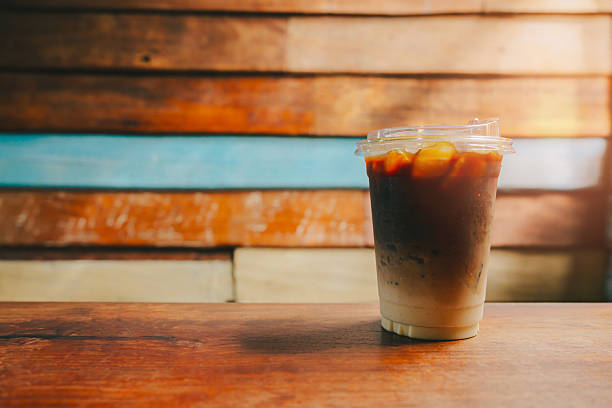 Ice coffee in cafe. Refreshing Iced Coffee in Clear Plastic Cup on Rustic Wooden Table with Colorful Background