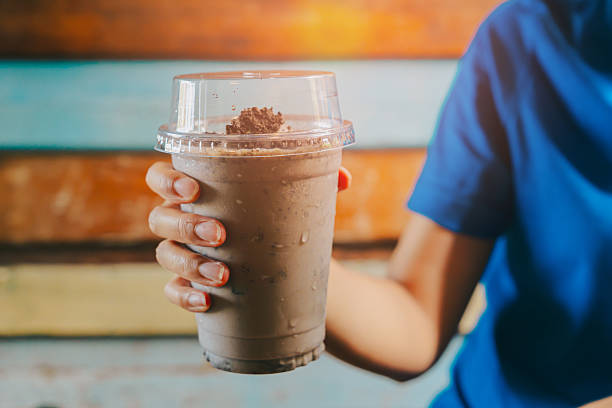 Chocolate Smoothie. Delicious Milkshake in a Clear Cup Held by a Person with a Blue Shirt Against a Wooden Background