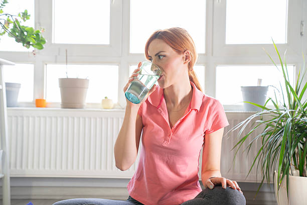 istock Young woman drinking water after exercise at home 2221921437