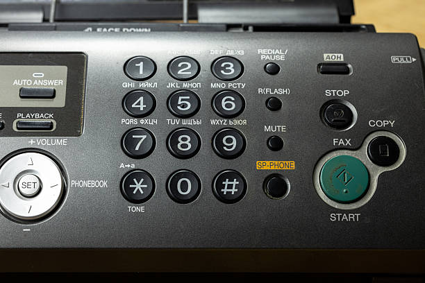 A close-up of a retro telephone with an answering machine. The device features a numeric keypad, buttons for functions like fax and copy, and a green start button.