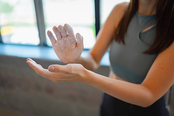 Close-up of a young female athlete applying climbing chalk to her hands in preparation for a session at an indoor bouldering gym. The chalk dust floats in the light, capturing a moment of focus, readiness, and tactile ritual before physical effort. This image highlights the details and mental preparation behind climbing sports.