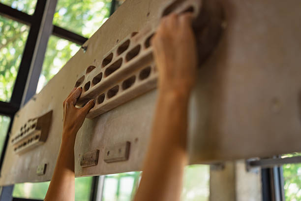 Close-up image of a female athlete’s hand gripping a wooden hangboard during climbing-specific strength training. The photo emphasizes finger tension, muscle definition, and the texture of the training equipment, capturing a moment of focus and physical control. Natural light highlights the grip technique and functional training detail.