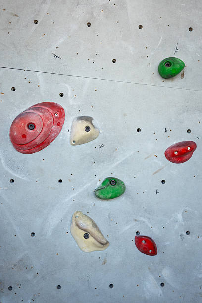 Minimal close-up of colorful indoor climbing holds mounted on a light grey bouldering wall. The holds vary in shape, texture and color. Shot in a modern climbing gym with soft natural light.