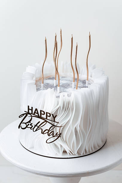 Luxury birthday cake with white chocolate and fondant icing decorated with edible paper and golden candles on the white background. Beautiful white anniversary cake for a lady