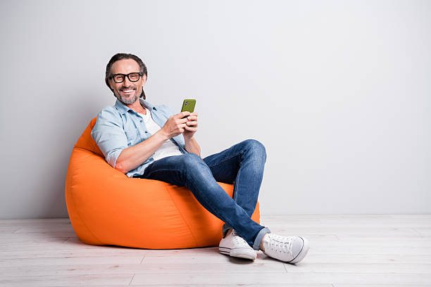 Profile side view of handsome cheerful mature man sitting on bean chair using device browsing isolated over grey pastel color background
