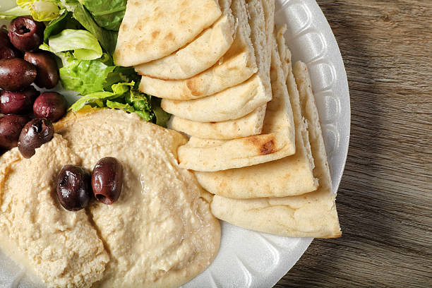 Close up hummus dish with olives and pita bread