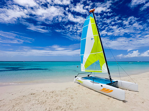 A vibrant catamaran rests on the pristine white sands of Grace Bay Beach in Providenciales, Turks and Caicos. The turquoise waters stretch to the horizon under a striking blue sky scattered with textured clouds, capturing the essence of a perfect Caribbean day.