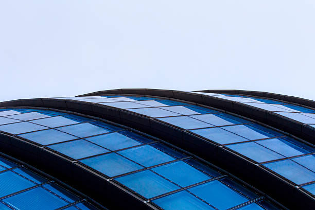 Close-up view of a modern curved building with blue glass panels and sleek architectural lines. The minimalist design and abstract angle make it perfect for concepts like innovation, corporate identity, and urban development.