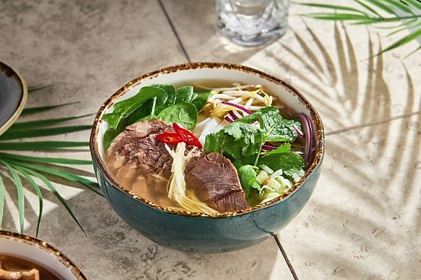 istock Pho bo soup with beef, herbs, and noodles in bright sunlight, overhead minimal composition 2221987706
