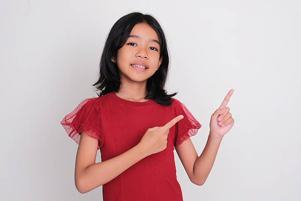 istock Asian kid girl smiling at the camera while pointing beside her 2221990117