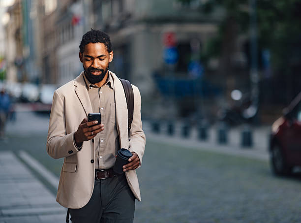 istock Businessman Walking Outdoors Using Smartphone Holding Coffee Cup in Urban Street 2222011190