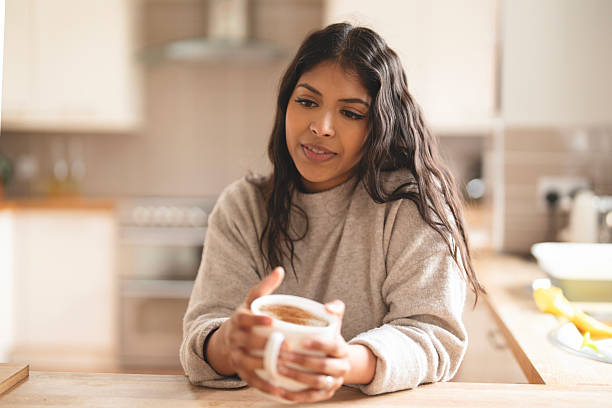 Young woman enjoys warm beverage in cozy kitchen while lost in thought during daytime