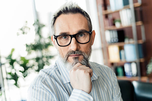 istock Confident professional man with glasses and gray beard in a modern office setting, indoors with a thoughtful pose 2222016217
