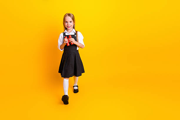 istock Happy schoolgirl in uniform holding a learning tool against a vibrant yellow backdrop with joyful and energetic vibes 2222026517