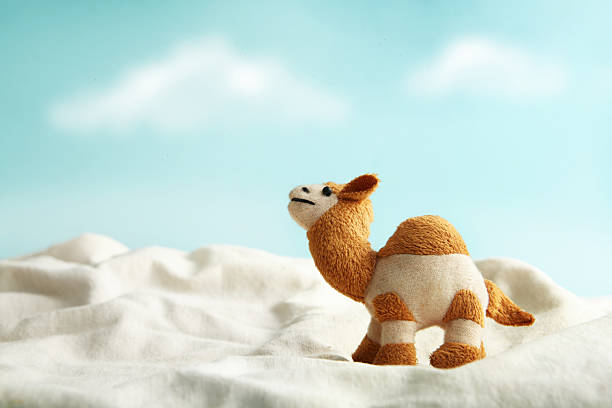 Mini camel doll toy on crumpled cloth on cyan background with clouds