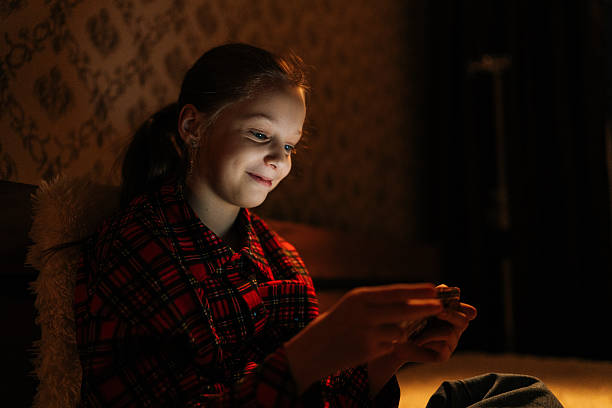 istock Happy smiling 10s girl using mobile phone, light screen glowing on face, sitting alone in dimly lit bedroom during late evening hours, engrossed in digital world 2222030964