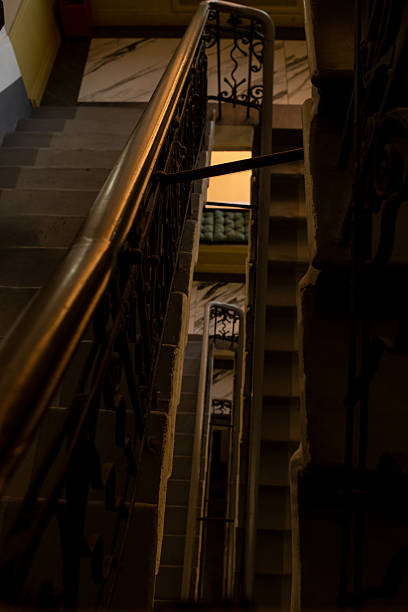 An ornate staircase with detailed railing leads downward within a historic structure, illuminated softly by ambient light, suggesting a cozy atmosphere.