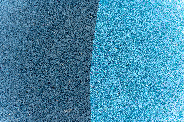 Close-up of a two-tone rubberized playground surface in dark and light blue. The texture provides shock absorption for safety during physical activity.
