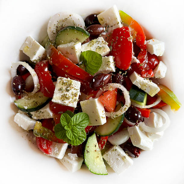 Greek salad with feta cheese and fresh vegetables like tomatoes, pepper, cucumber, onion, olives, origano on a white background. Greek cuisine. Healthy and vegetarian food. Directly above.