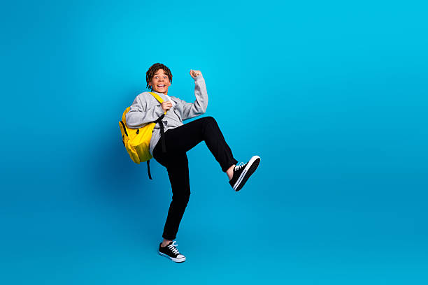 istock Joyful student in casual attire with yellow backpack celebrates on a bright blue background symbolizing academic success 2222040278