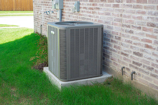 istock Small landscaping shrub, grassy yard and central air conditioning condenser unit mounted on concrete slab beside brick house wall, utility meters and electrical disconnect, suburbs Dallas, Texas 2222043563
