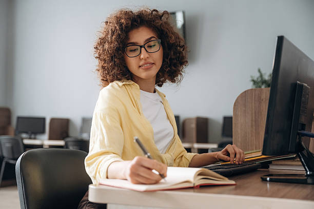 istock Making information research, with notepad and pen. Woman is in the library section with computers 2222046986