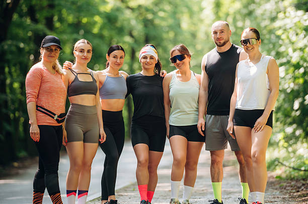 Two happy motivated fit young couples giving a thumbs up of approval and success and they pose in their sportswear in a park smiling at the camera