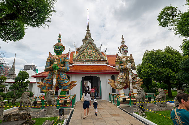 Bangkok, Thailand - July 17, 2024: Colorful temple entrance with traditional guardian statues and richly decorated rooftops at a temple near Wat Arun, capturing Bangkok�s ornate architectural identity.