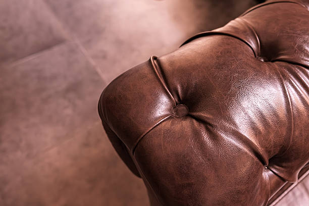Close-up of brown leather chesterfield sofa armrest. The natural creases of showcasing the quality and luxury of classic interior furniture design. Selective focus.
