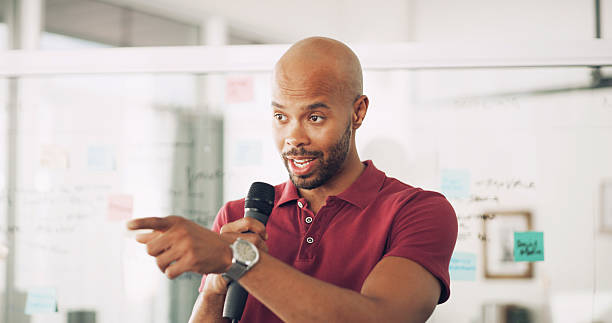istock Presentation, speaker and man with mic, confident and information for seminar, training and talking. Business, employee and black person with speech for workshop, pointing or tech for public speaking 2222069292