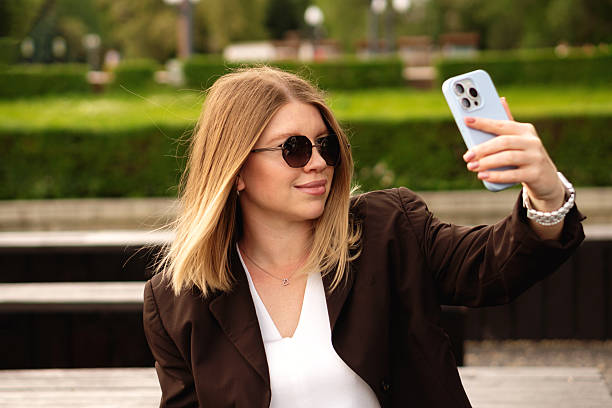istock Young woman posing for selfie with smartphone outdoors in brown jacket 2222070127