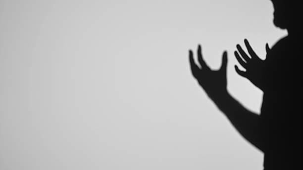 istock Shadow Silhouette of Raised Hands on a Light Background 2222072547