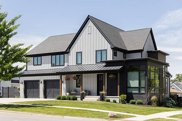 Barrington, IL, USA - June 11, 2024: A modern farmhouse with white and black siding, a covered front porch, and two car garage with black doors.