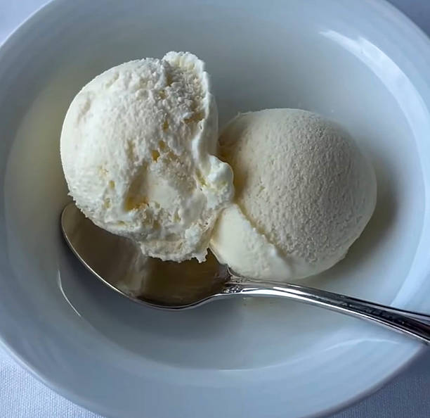 istock Delicious Vanilla Ice Cream Scoops in a White Bowl with Silver Spoon, on a soft fabric surface 2222077548