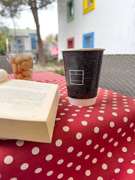 Take away Coffee Cup on Polka Dot Tablecloth with opened Book and Biscuits over colorful Urban Courtyard