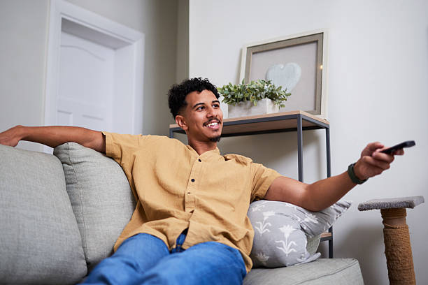 istock Relaxed Man Sitting on Couch Holding TV Remote and Smiling in Comfortable Home Setting 2222087413