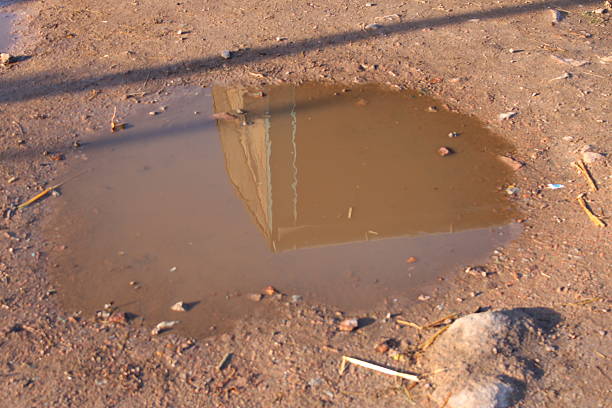 Reflection of a Building in a Small Muddy Puddle on Dirt Ground