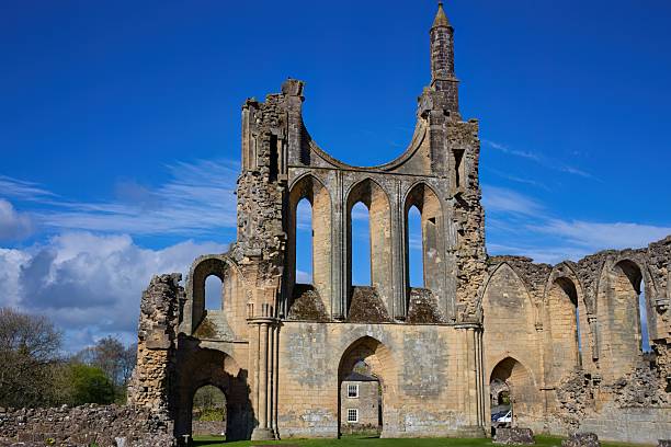 istock Gothic-style stone ruins with towering arched windows, sunlight casting shadows through openings, and a vibrant blue sky 2222088460