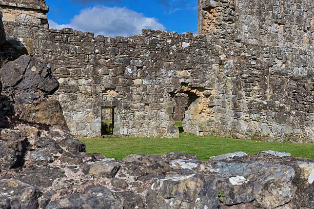 The image shows a weathered stone ruin with green grass growing inside and a patch of blue sky visible through a hole at Byland Abbey - North Yorkshire - United Kingdom