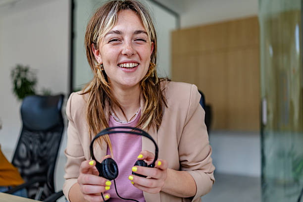 istock Young adult woman smiling while using headphones in a modern office environment during work hours 2222090623